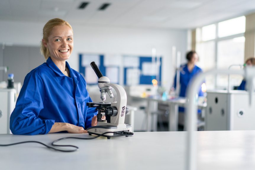 Female Science student wearing blue lab coat using a microscope in a science lab
