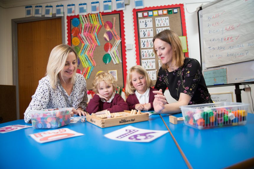 Two female Early Years Education students sat with two primary school-aged children doing learning activity