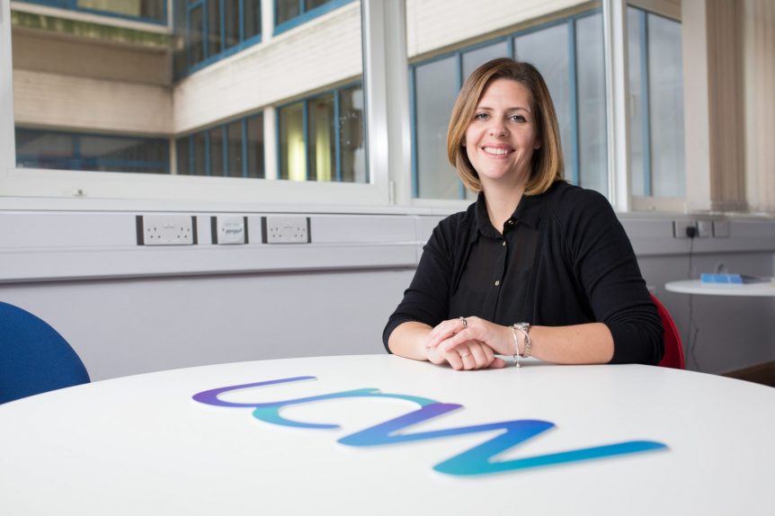 Female SEND and Inclusive Practice student sitting at a UCW branded table and smiling at the camera