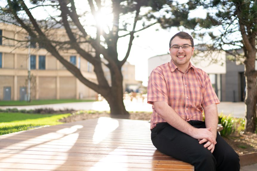 Male Education and Early Years student smiling with University campus in the background