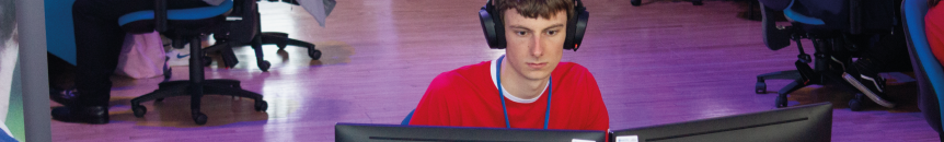 Male Computing student wearing headphones and working on two computer monitors