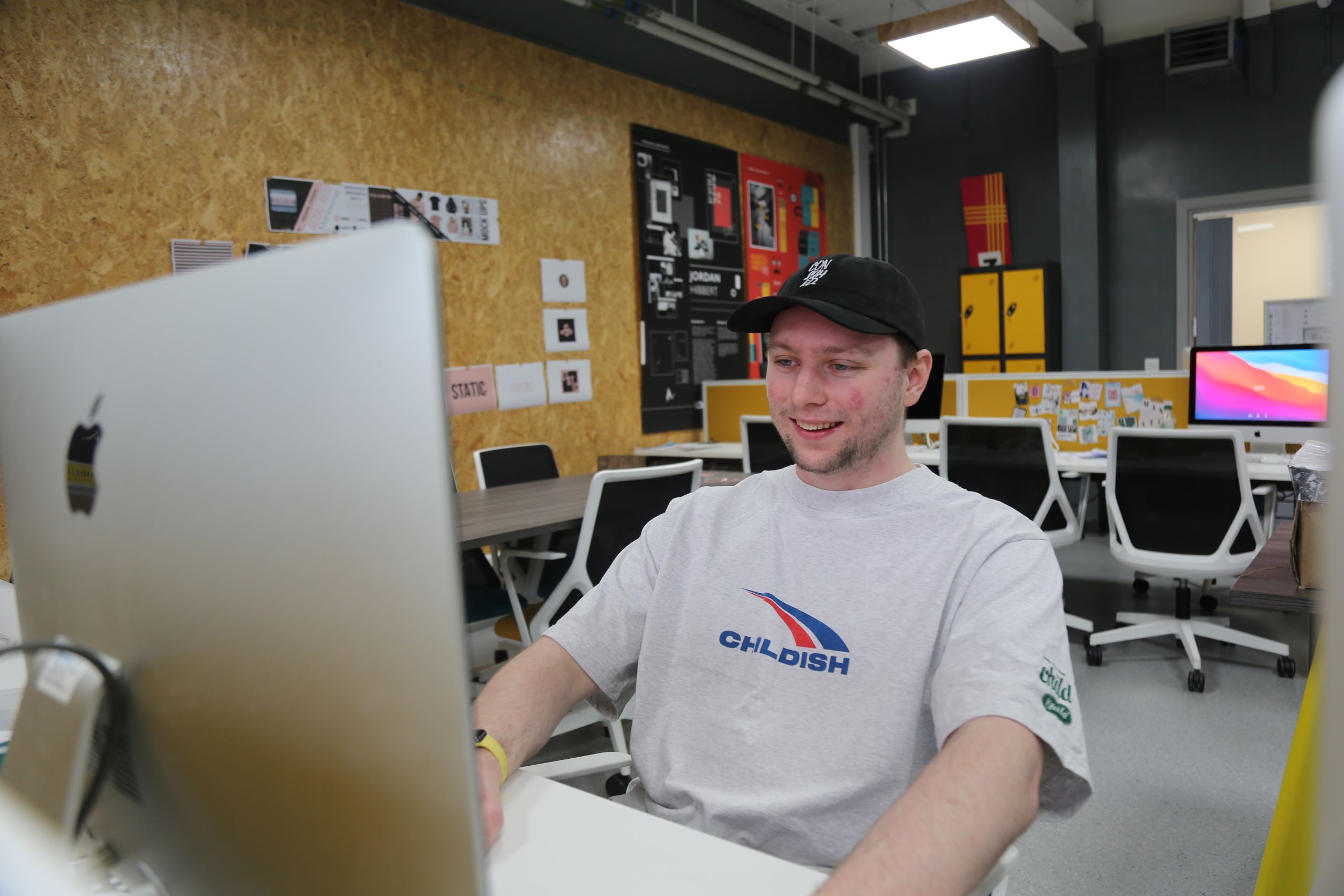 Dan smiling at computer screen sat in yellow modern design studio