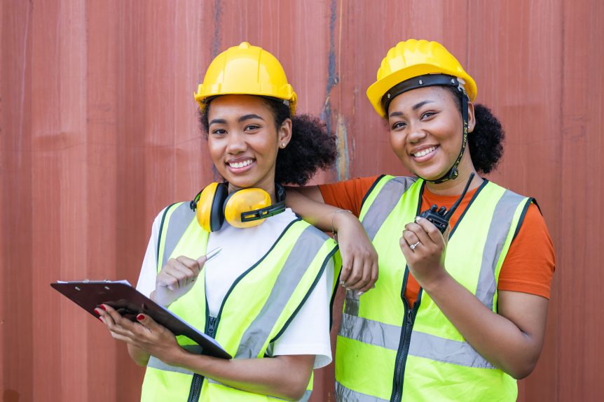 2 female construction workers wearing hard hats and high vis jackets, one holding a clipboard