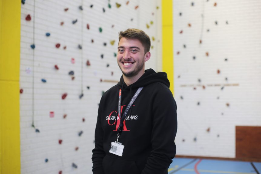 Male Uniformed and Public Services student standing in front of rock climbing wall in a sports hall