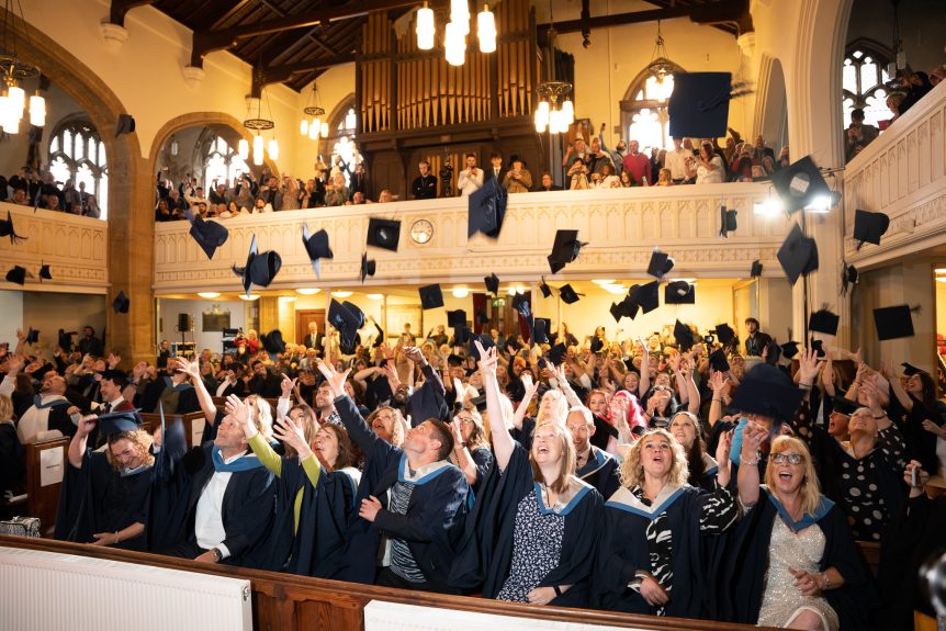 students inside church throwing graduation hats in the air