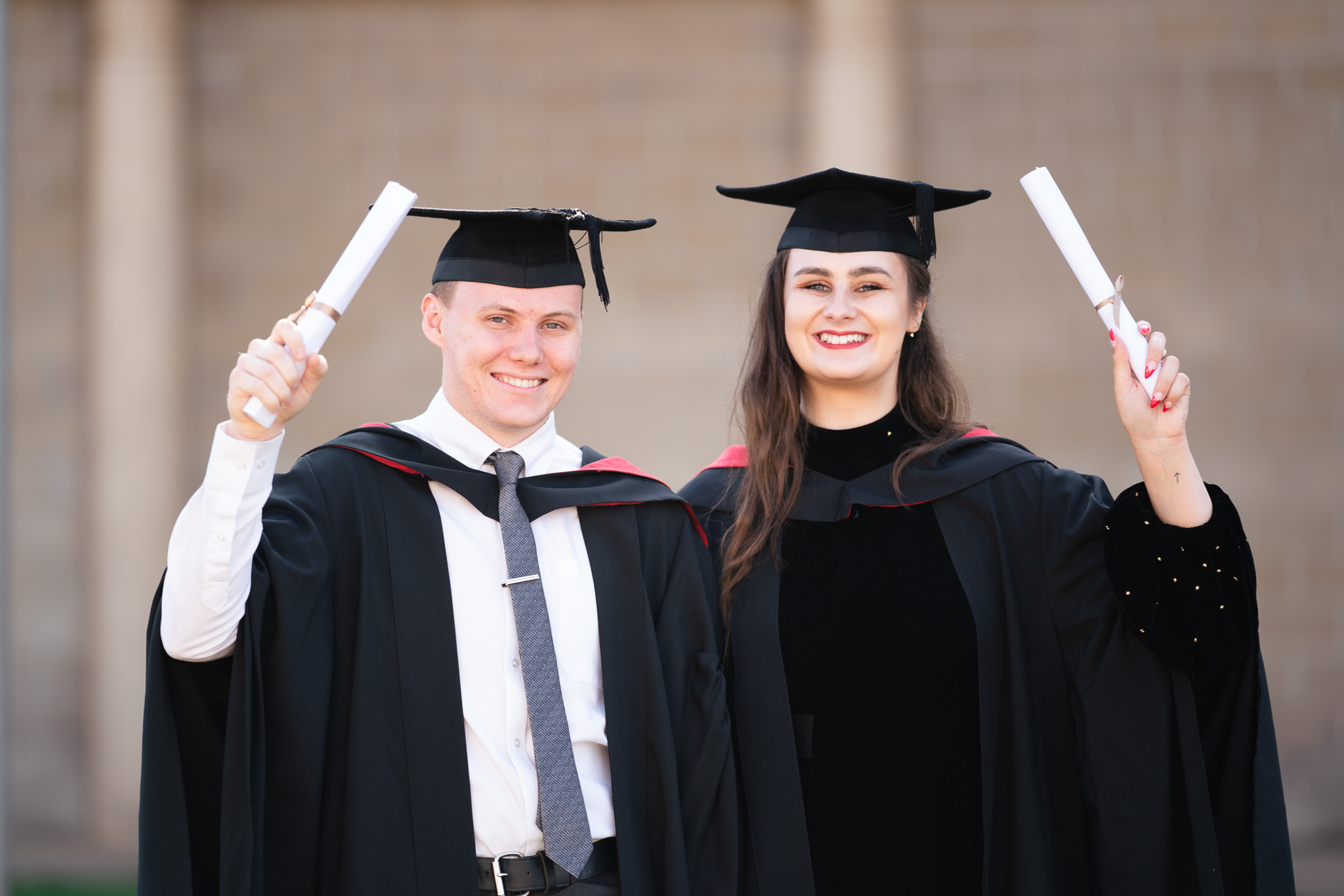 2 graduates holding up their scrolls