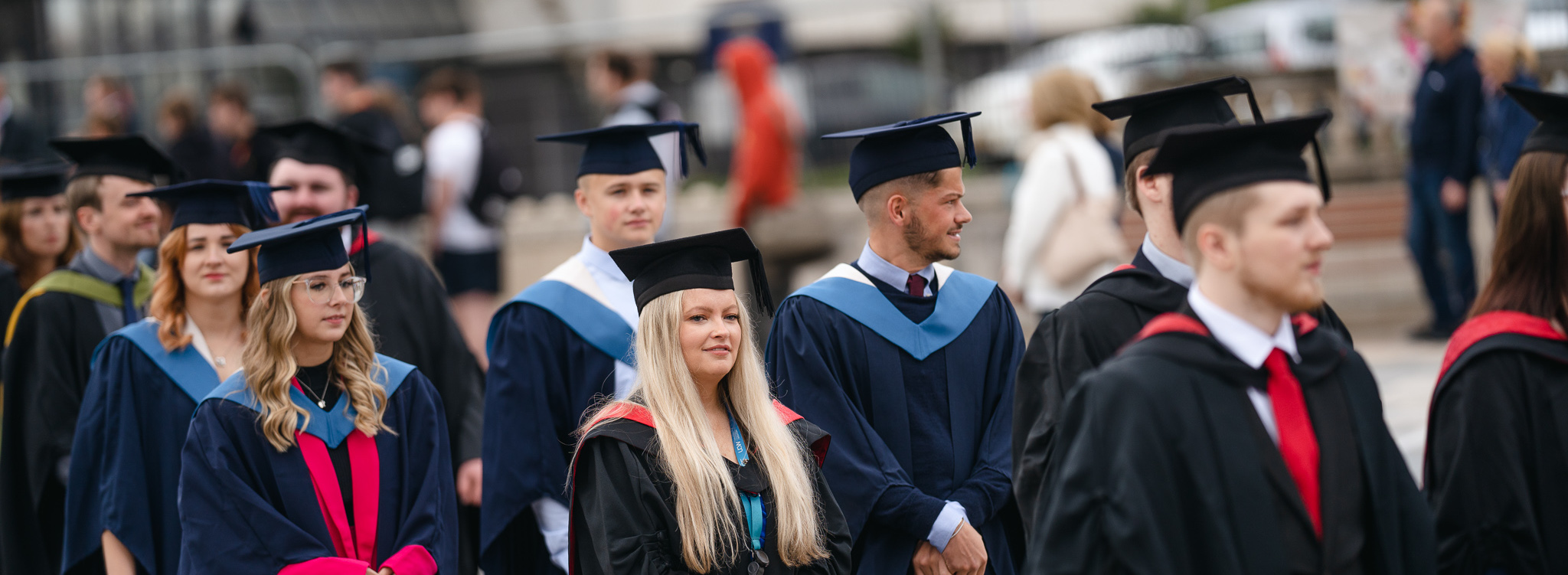 students in graduation gowns stand in a line while walking to the ceremony