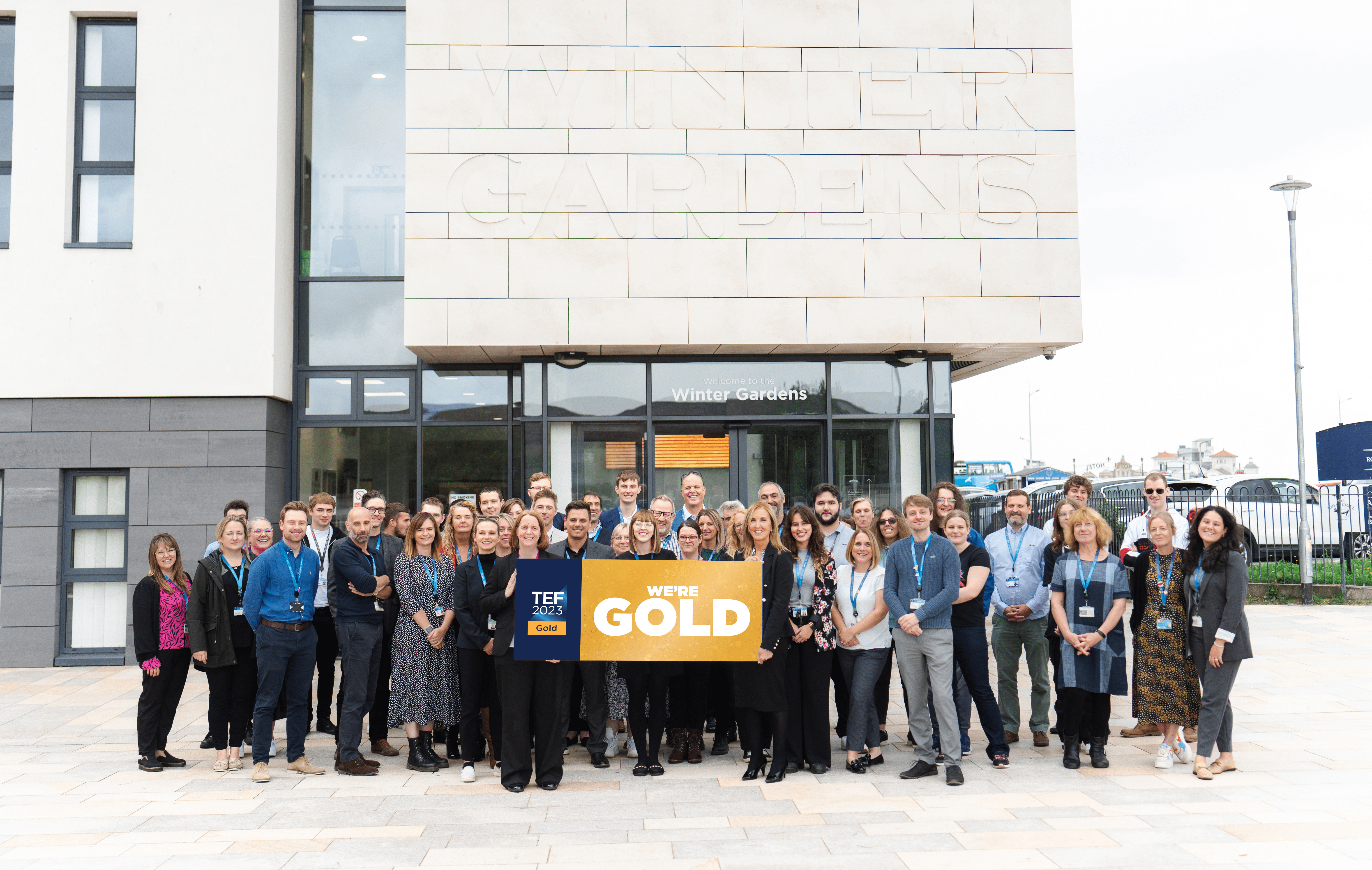 University staff holding TEF GOLD sign outside Winter Gardens campus